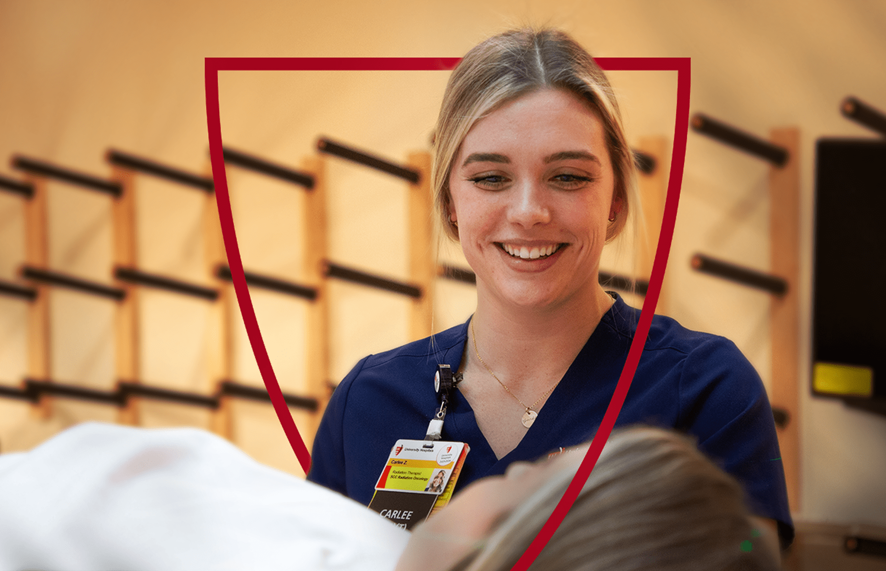 A smiling healthcare professional in navy scrubs interacting with a patient in a medical setting.