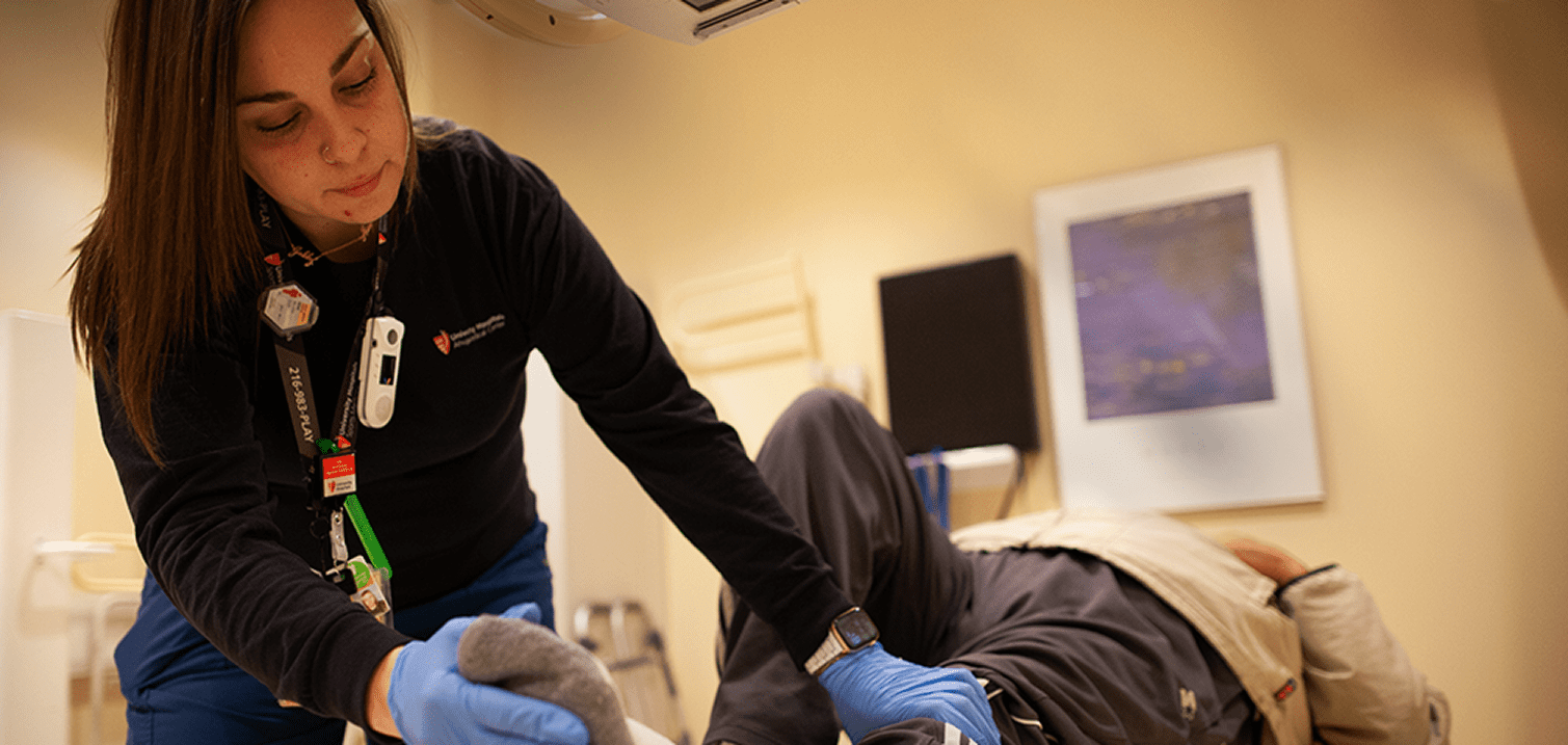 A healthcare professional assists a patient lying down, focusing on their care in a medical setting.