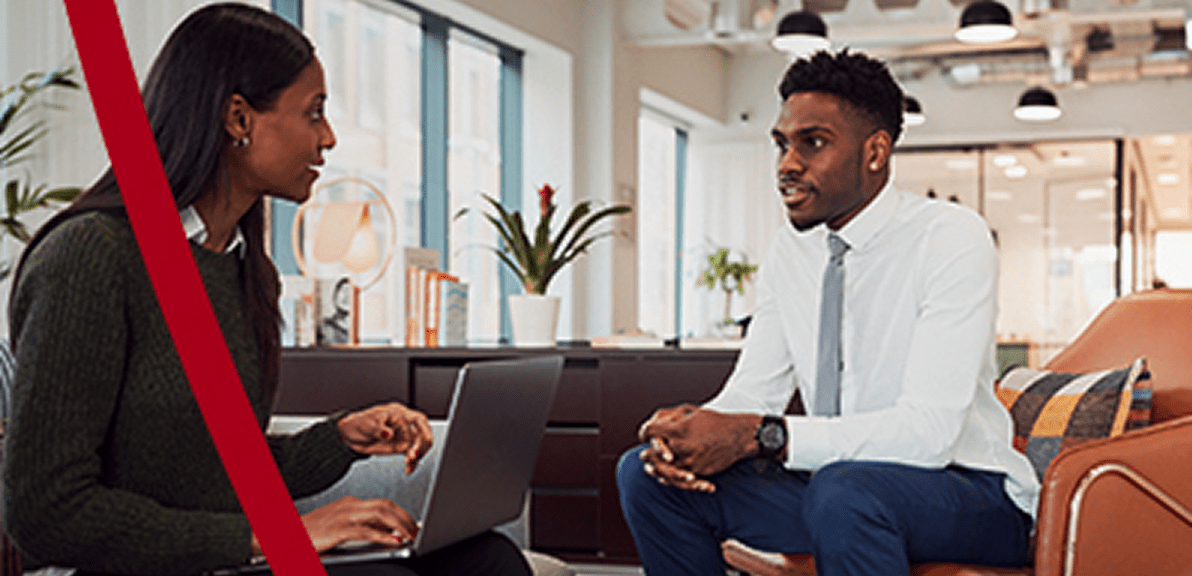 Two professionals in a modern office sit engaged in a conversation.