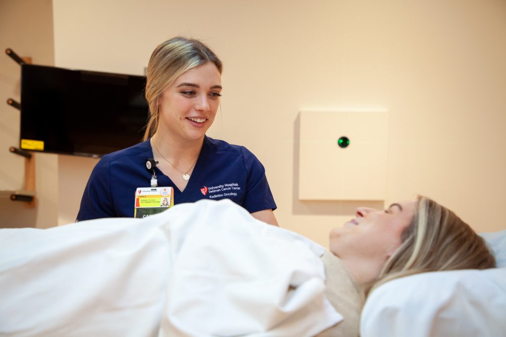 3e1df3152339f785cfbdfbf2585ecce29622699b A smiling healthcare professional in navy scrubs interacting with a patient in a medical setting.