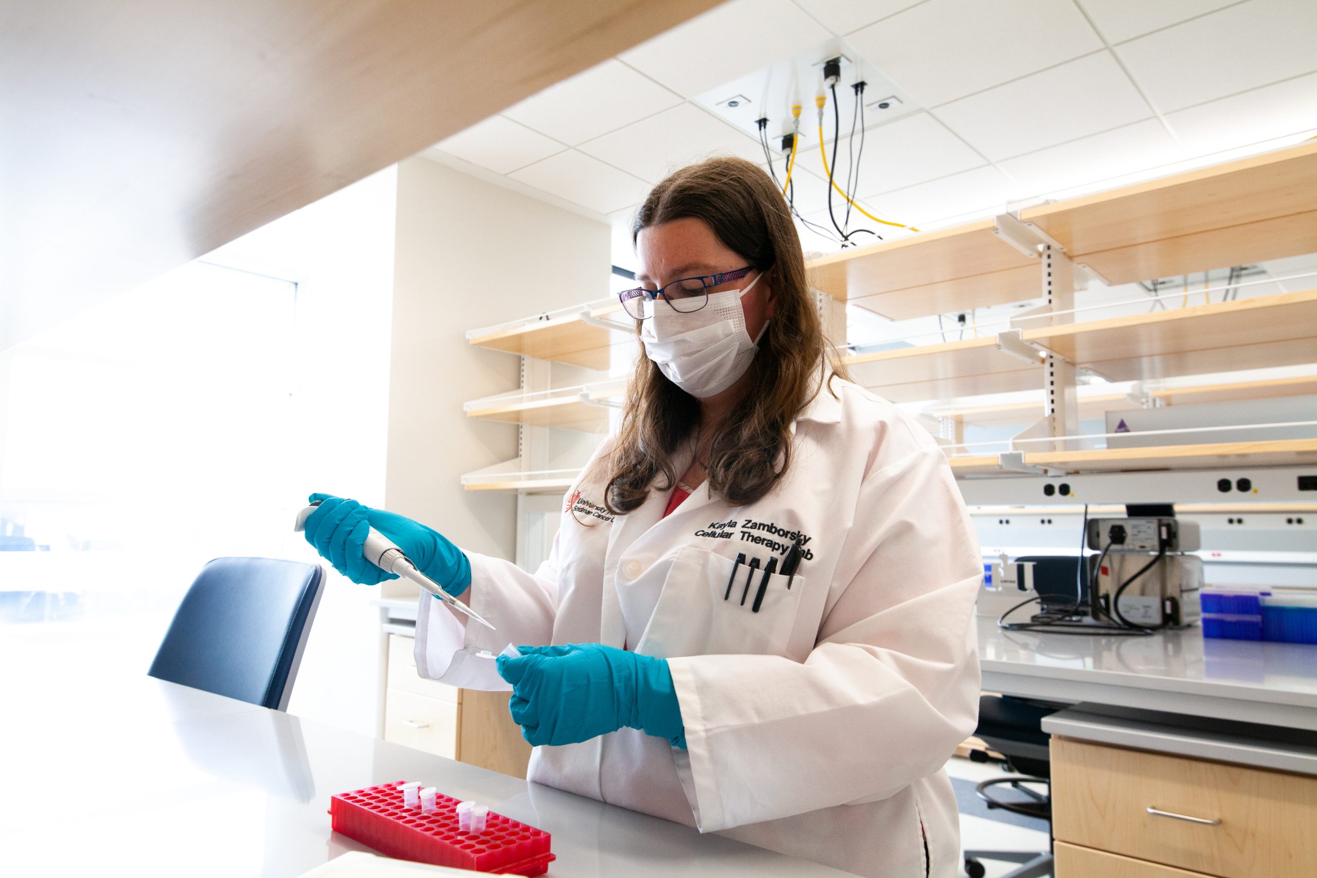 e88e376dd6e921514d2795f798387ab4c2ae98fd A scientist in a lab coat and gloves using a pipette while working in a research laboratory setting.