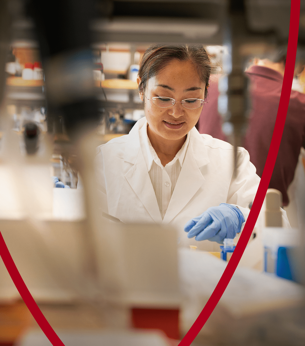 c6d532ced5aab74fee56421917b4d1add21b759d A scientist in a white lab coat and gloves conducts research in a laboratory, focusing on an experiment.