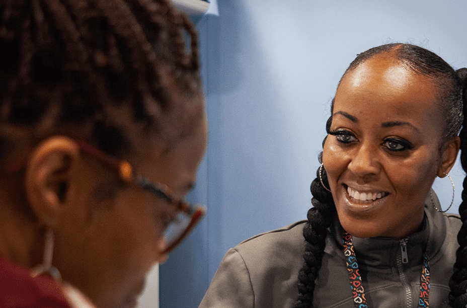 A friendly healthcare worker in a gray uniform engages in conversation with a colleague in a welcoming clinical environment.