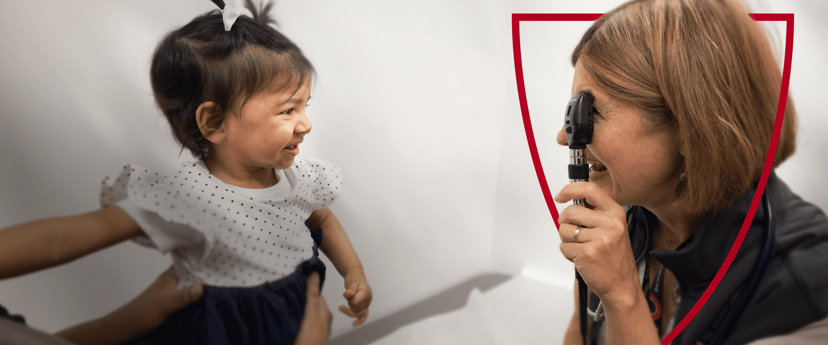 A smiling healthcare professional examines a young patient's eyes with an ophthalmoscope.