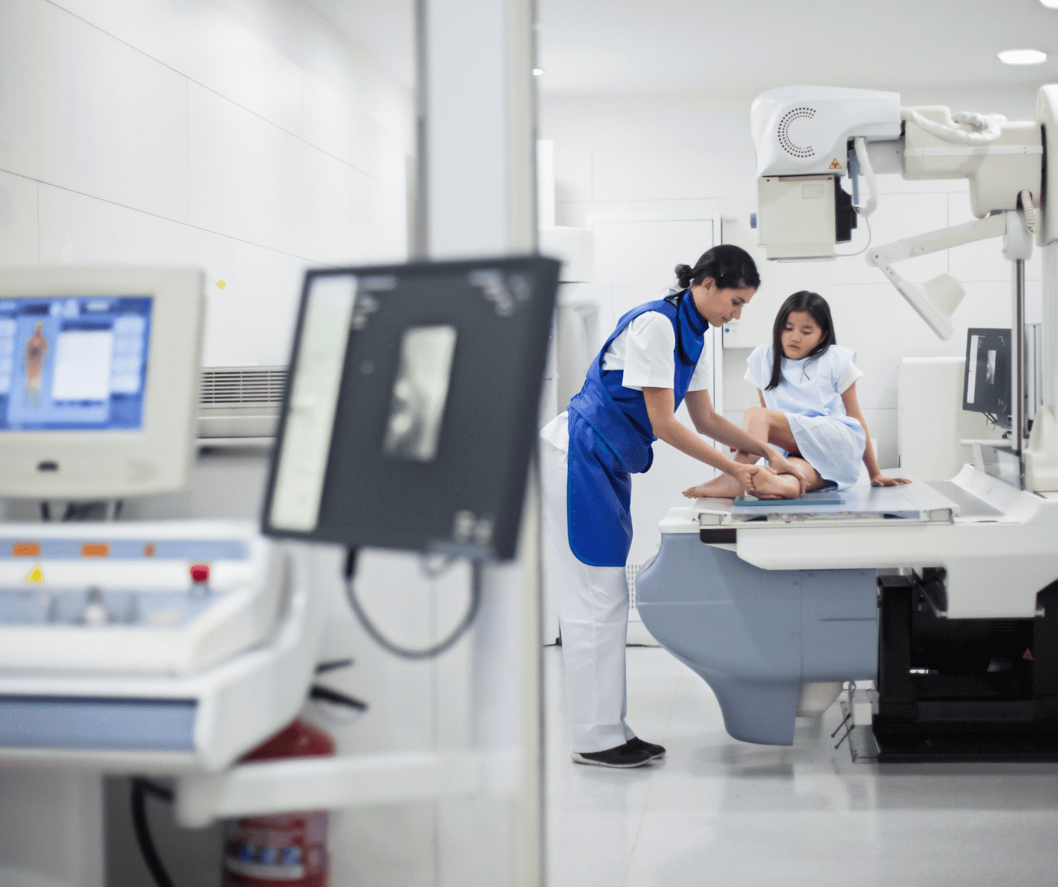 Radiology technologist positioning a young patient on an imaging table inside a brightly lit medical imaging room, preparing for a scan.